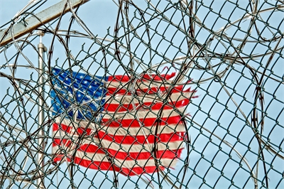 American flag pictured behind barbwire and a chain-link fence American flag pictured behind barbwire and a chain-link fence
